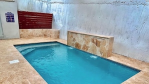 Une piscine intérieure rectangulaire, bordée de pierres et dotée d’un banc rouge.