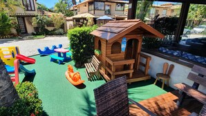 Uma área de recreação infantil com escorrega, baloiços e um pequeno pavilhão de madeira.