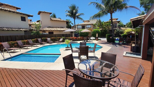 Uma área de piscina com espreguiçadeiras e uma mesa, cercada por palmeiras e um deck de madeira.