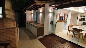 Uma cozinha moderna com estrutura de vidro, um banco de madeira e um forno de tijolos.