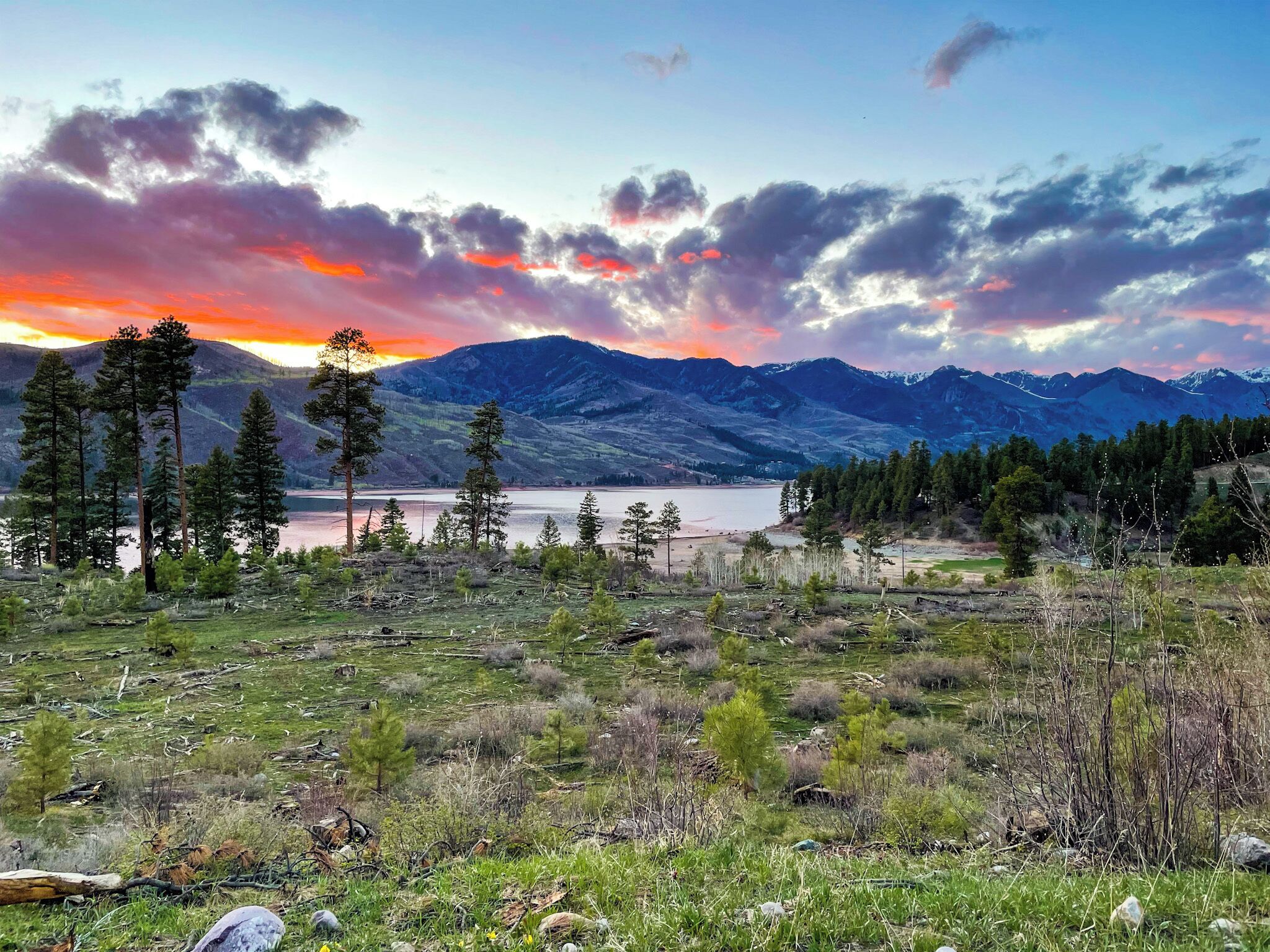 A mountainous landscape with a lake, trees, and a clear sky.
