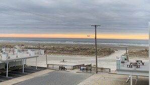 Un aparcamiento junto a la playa con un banco y un cartel, con vista al océano bajo un cielo nublado.