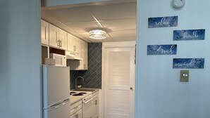 Una cocina compacta con armarios blancos, microondas integrado y pileta de acero inoxidable. Se observan elementos decorativos en la pared con palabras como 