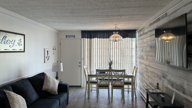 Una sala de estar con un sofá azul oscuro, una mesa de comedor con sillas, una lámpara colgante y un cartel en la pared.