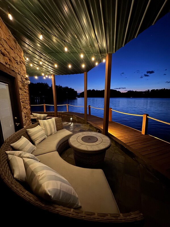 An outdoor seating area with a curved sofa and a round table, overlooking a body of water.