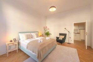 Un dormitorio con cama, mesita de noche, lámpara, silla y vistas a la cocina.
