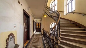Un couloir doté d’un sol à carreaux, d’une porte en bois et d’un escalier orné de rampes en métal.