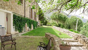 Un edificio de piedra con un patio cubierto de césped, un banco y una planta en maceta.