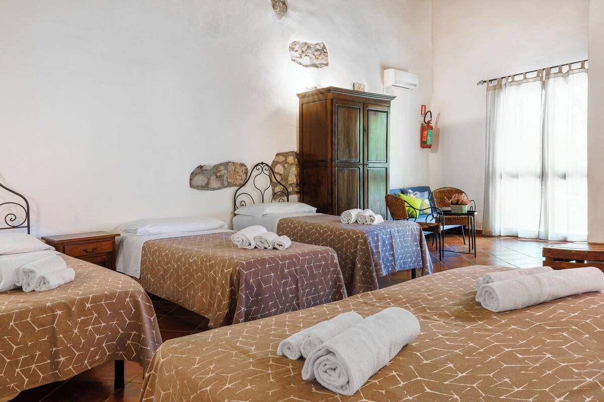 Una habitación de hotel con tres camas, un armario de madera, una silla y una ventana con cortinas.