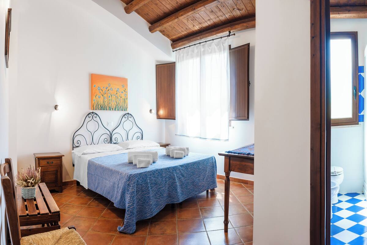 Un dormitorio con cama, mesita de noche y ventana con cortinas.