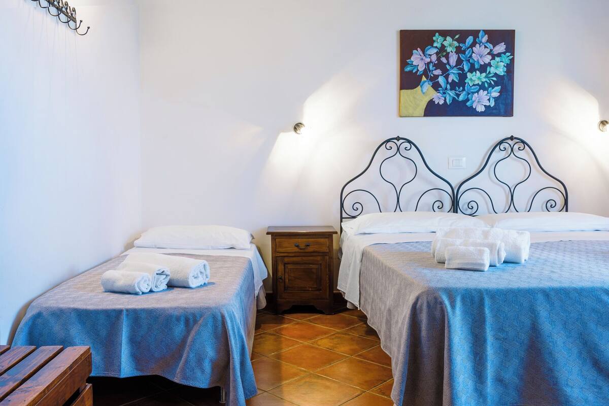 Una habitación de hotel con dos camas individuales, una mesita de noche de madera, una pequeña mesa y un cuadro en la pared.