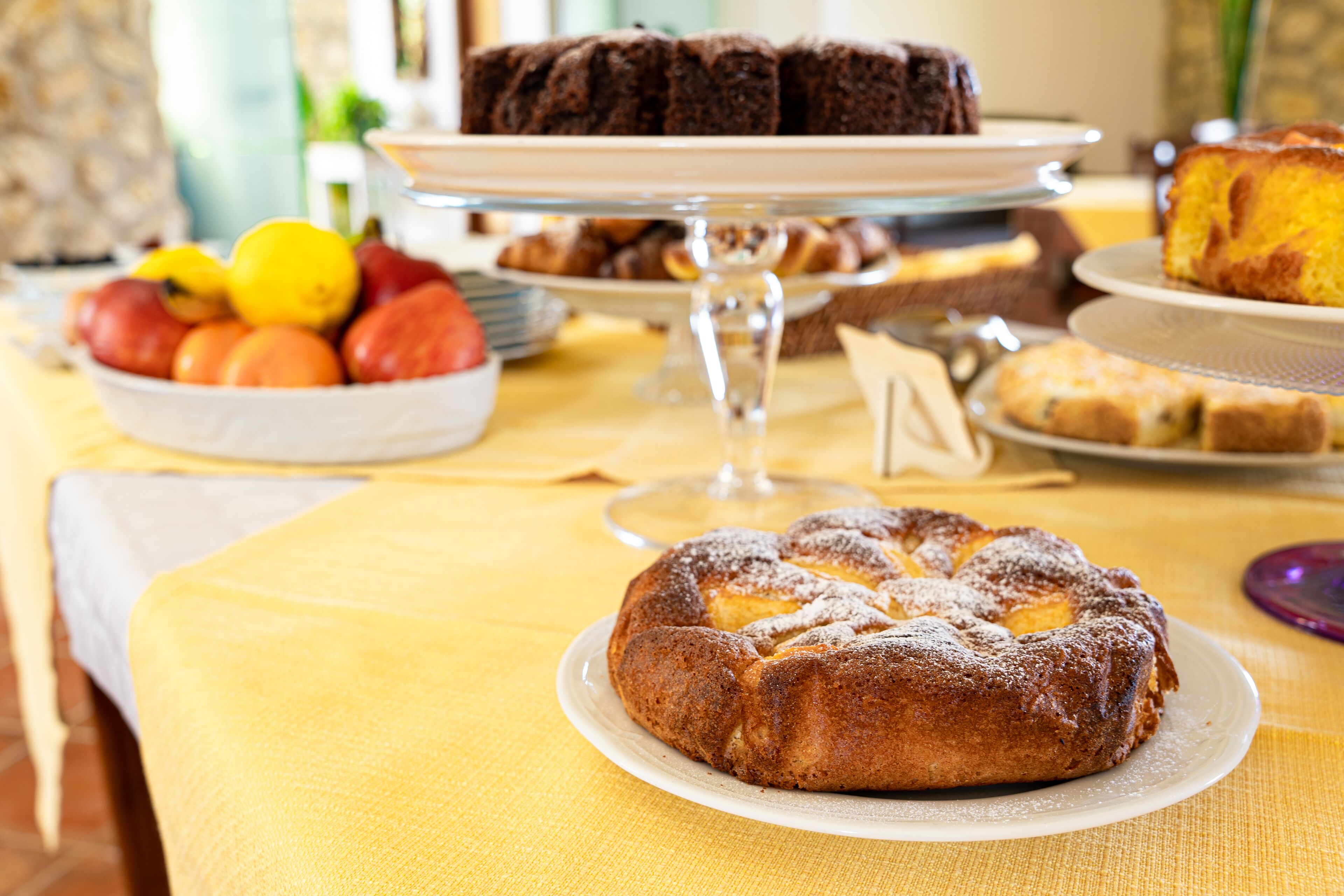 A table with various baked goods, including a cake and pastries, on a yellow tablecloth.