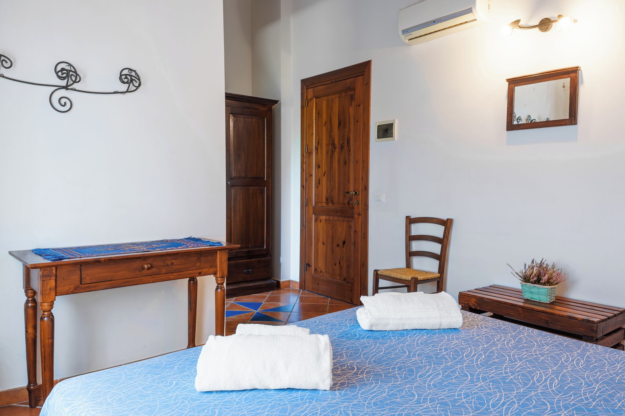 Ein Schlafzimmer mit einem Bett, einem hölzernen Schreibtisch, einem Stuhl und einem kleinen Tisch mit einer Pflanze.