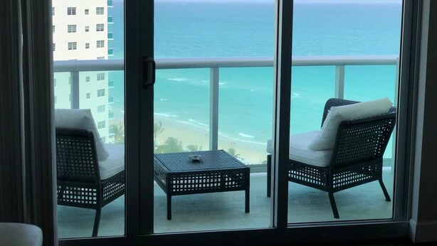Un balcon avec deux fauteuils en osier et une petite table, donnant sur une plage et l’océan.