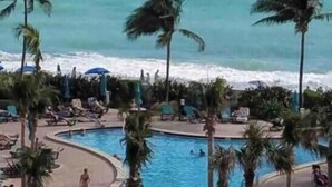 Un espace piscine situé au bord de la plage, agrémenté de palmiers et offrant une vue sur l’océan.