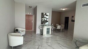 Un salon moderne avec un sol en marbre, une table basse en verre, un canapé blanc et une petite table ronde.