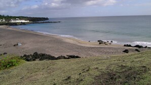 A beach with a rocky shoreline, a few buildings in the background, and a clear sky. - Villa Pópulo 5 min. from the beach (ponta delgada)