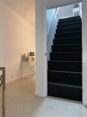 Un escalier menant à l’étage supérieur, une petite table avec une lampe et un mur blanc.