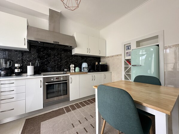 A modern kitchen with white cabinets, a black marble backsplash, a built-in oven, and a dining area with a wooden table and teal chairs.