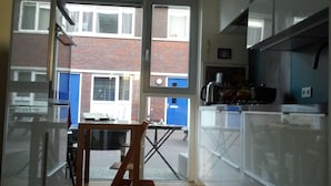Een moderne keuken met witte kastjes, een houten eettafel en uitzicht op een bakstenen gebouw.