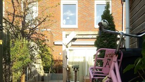 Een roze fiets geparkeerd in een tuin, met een huis van baksteen op de achtergrond.