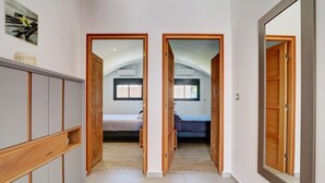 A hallway with wooden doors leading to a bedroom with a bed and a window.