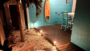 A wooden deck with a bench, a surfboard, and a small table.