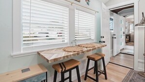 A kitchen with a wooden countertop, two stools, and a window with blinds.