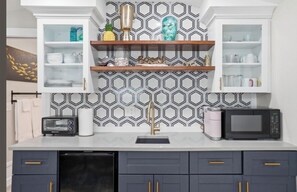 Una cocina con un salpicadero de diseño, armarios blancos, microondas, tostadora y lavavajillas.