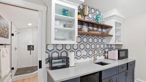 A modern kitchen with a microwave, toaster, and a sink. There are cabinets with gold handles and a patterned backsplash.