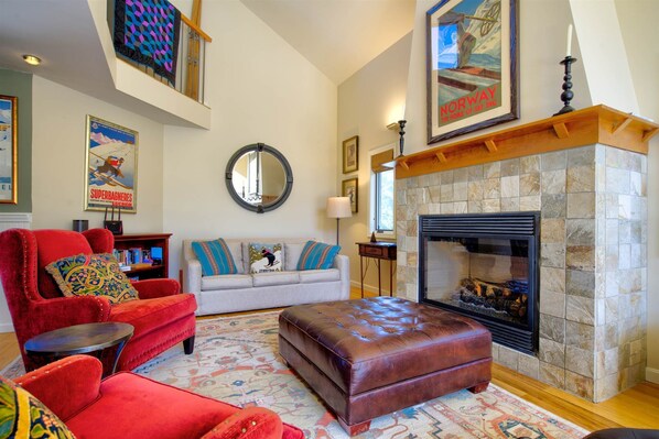 Un salón con chimenea, sillones rojos, un sofá blanco y una alfombra estampada.