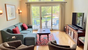 A living room with a sofa, two armchairs, a coffee table, a TV on a wooden cabinet, and a balcony with chairs and a table. - Extraordinary Stratton Ski On/Ski Off Home (Stratton)