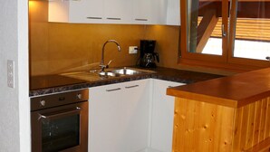 Una cocina compacta con armarios blancos, un lavamanos de acero inoxidable, horno empotrado y encimera de madera.