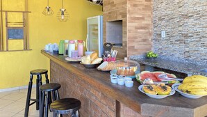 Angolo cottura con un bancone in mattoni, un frigorifero e una parete in pietra. Sono presenti degli sgabelli, un lampadario e diversi alimenti sul bancone.