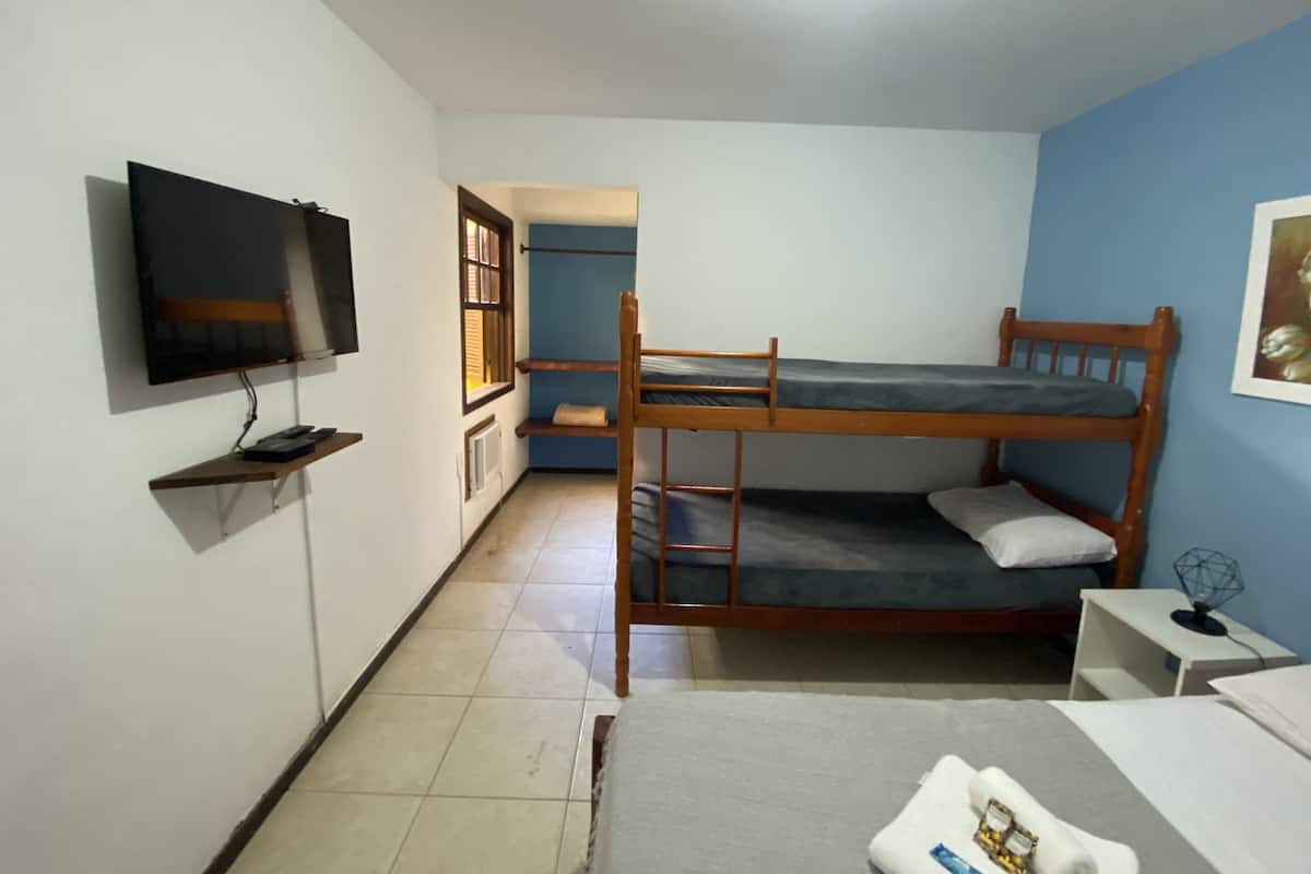 Una habitación con una cama litera, un televisor fijado en la pared, una mesita pequeña y una puerta que da a otra habitación.