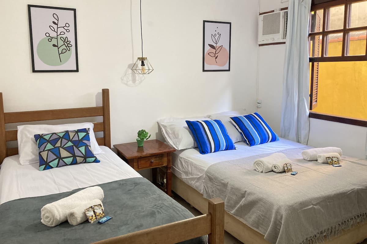 Habitación de hotel con dos camas, cada una con una almohada, una mesita con una planta y una lámpara fijada a la pared.
