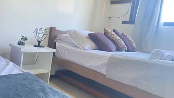 A bedroom with a bed, a bedside table with a lamp, and a window with curtains.