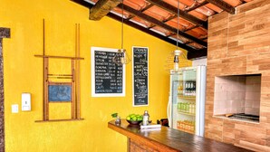 Angolo bar con parete gialla, menù scritti su lavagna, bancone in mattoni e forno a legna.