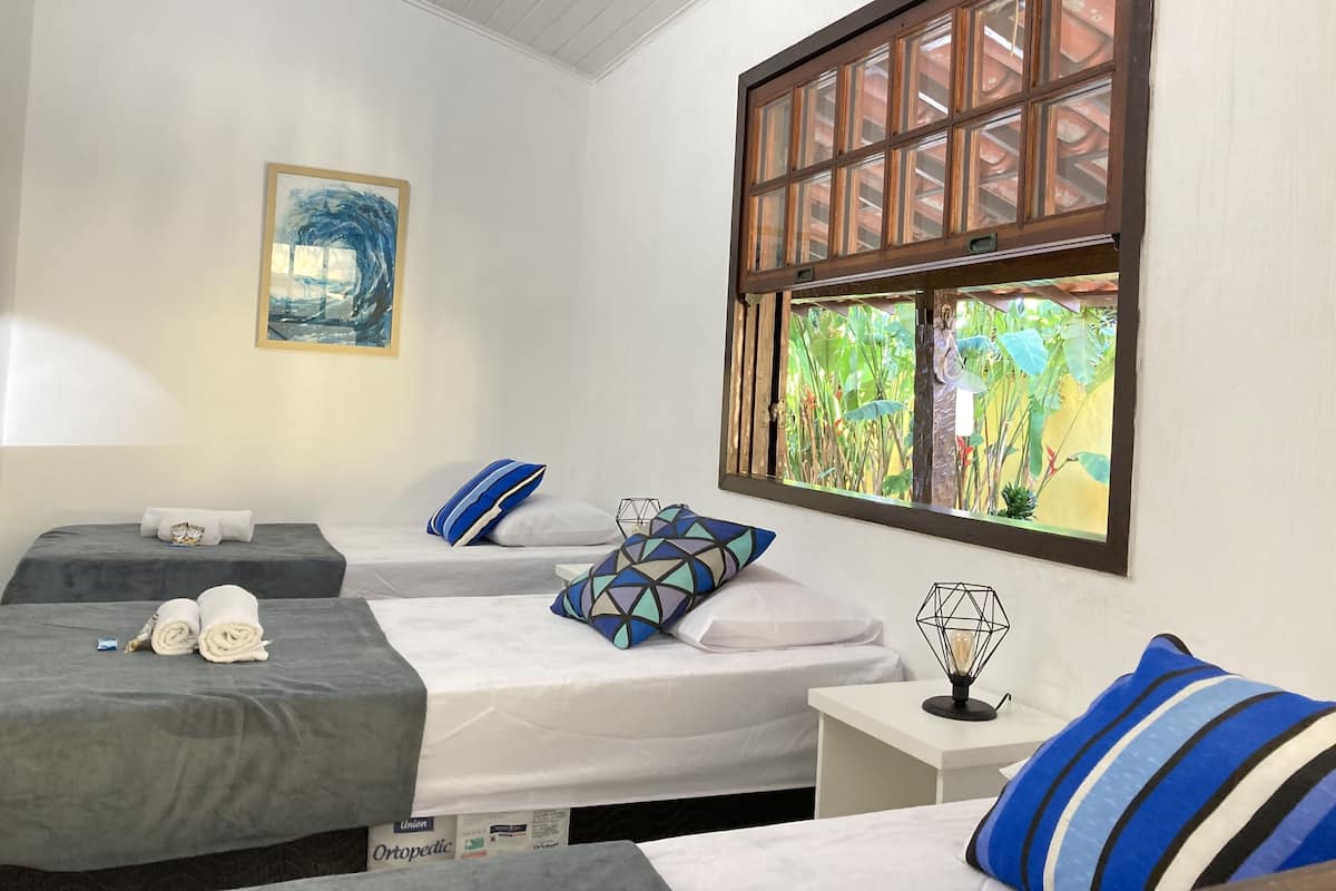 Habitación de hotel con dos camas, un cuadro, una ventana con vistas a vegetación y una lámpara de noche.