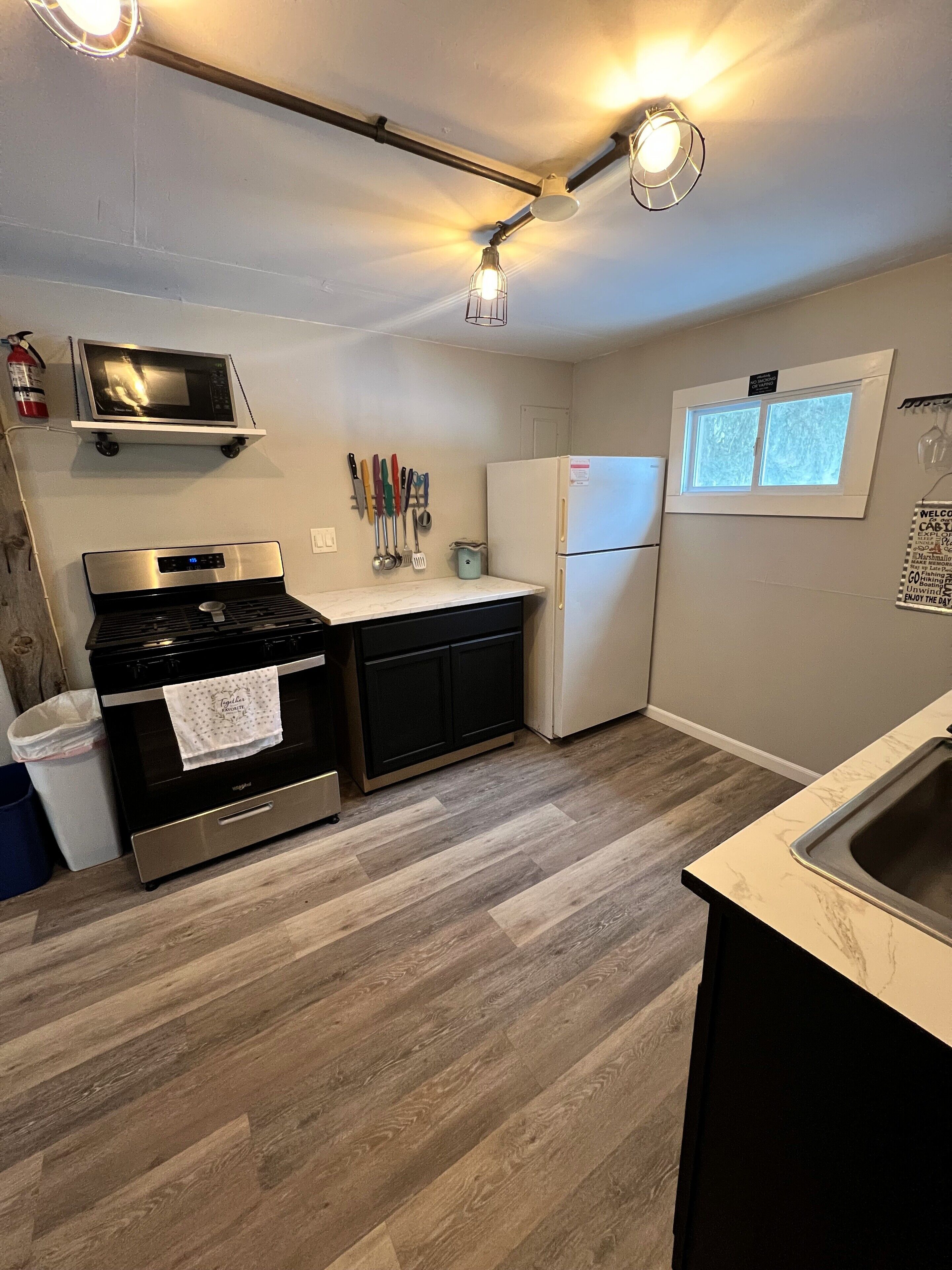 A compact kitchen with a stove, microwave, refrigerator, and a window.