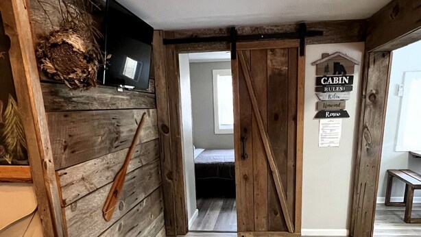 A room with a wooden floor, a bed, a TV, and a sign with 'CABIN RULES'. - Trails Head Cabin (Rock Hill)