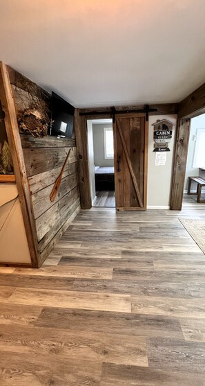A room with a wooden floor, a bed, a TV, and a sign with 'CABIN RULES'. - Trails Head Cabin (Rock Hill)