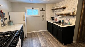 A kitchen with a stove, refrigerator, and wooden flooring. There are hanging utensils and a window with a view. - Trails Head Cabin (Rock Hill)