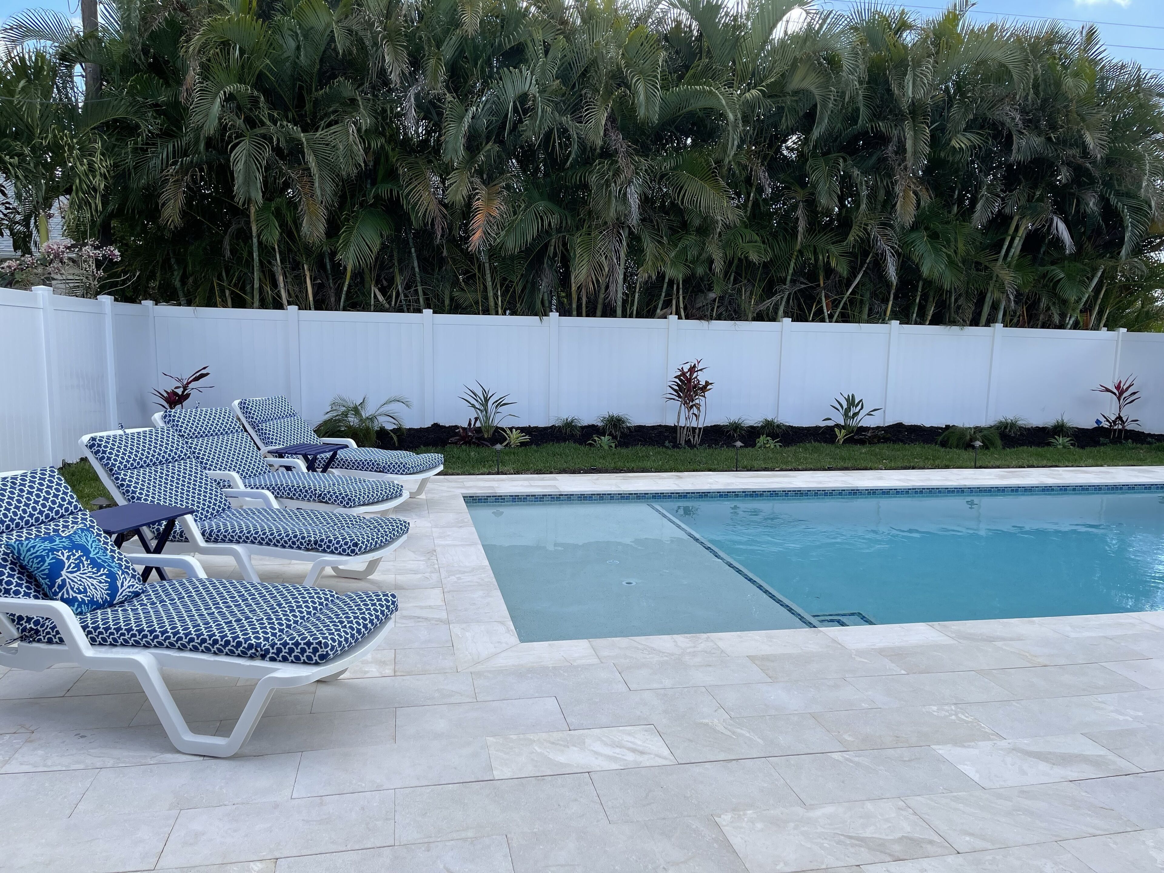 A pool area with lounge chairs and a white fence.