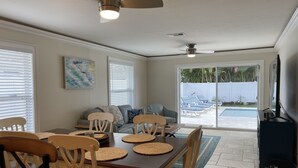 A dining area with a table and chairs, a ceiling fan, and a view of a pool through glass doors.