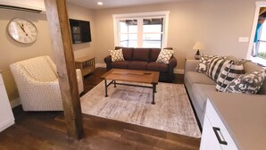 Een woonkamer met een bruine bank, een fauteuil met een patroon, een houten salontafel en een aan de muur bevestigde televisie.
