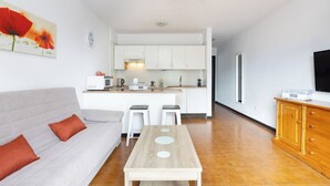 A modern living room with a sofa, a coffee table, and a kitchen area with white cabinets and a TV. - Home2Book Sunny Apt Pool & Terrace, Las Américas (Playa de la Américas)