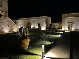 A courtyard with a large vase, a pathway, and a building with arched windows and a door.