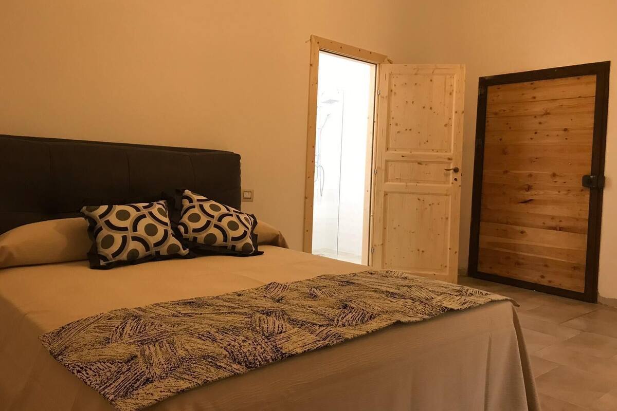 Ein Schlafzimmer mit einem Bett, Kissen, einer Decke, einer Holztür und einem Fenster.