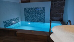 Een moderne badkamer met een houten vloer, een badkuip met mozaïektegels, en een handdoek op een houten bankje.